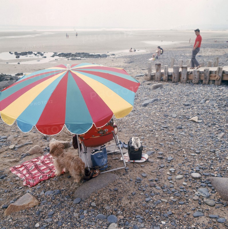 Dans les années 1970 sur une plage normande, vacanciers sous un parasol.
