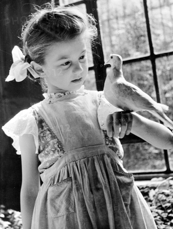 Enfants dans les années 1950. Mode et physionomie.  Petite fille portant une robe et des rubans dans les cheveux, s'amusant avec un oiseau.