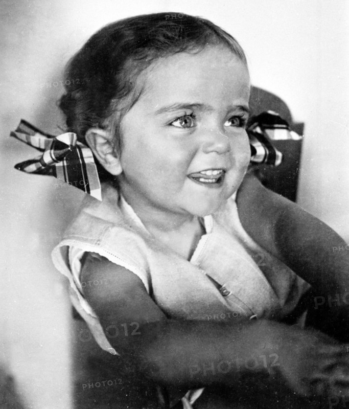 Mode et physionomie des enfants dans les années 1950. Les plaisirs des contes et histoires.   Petite fille vêtue d'une robe blanche portant des noeuds à carreaux dans ses cheveux.
