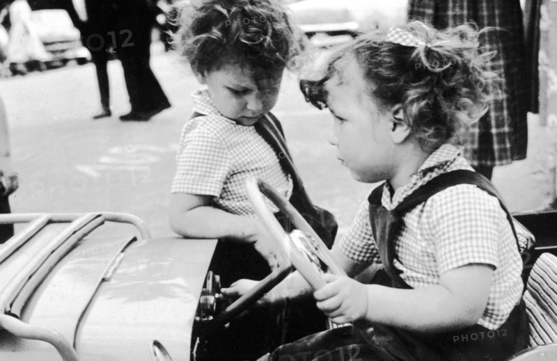 Mode et physionomie des enfants dans les années 1950. Concours d'élégance de l'automobile en 1952.  Le petite fille vêtue d'une salopette et d'une chemise participe au concours, aux côtés d'une autre petite fille.