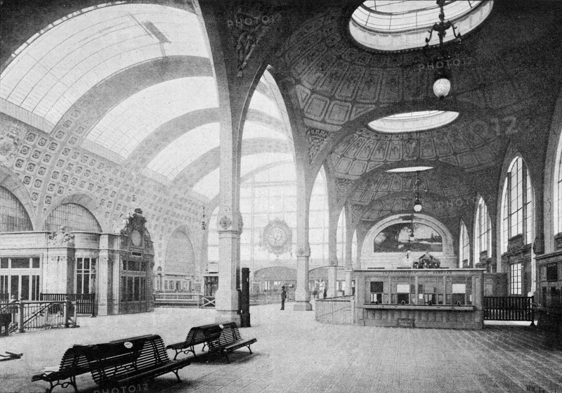 Septembre 1900, vue intérieure du rez-de-chaussée de la nouvelle gare de la Compagnie des Chemins de fer d'Orléans, quai d'Orsay à Paris.  "Toute l'ossature métallique est cachée par un second plafond, avec remplissage en verre et en staff. Dans le vestibule, ce second plafond se compose d'une série de coupoles éclairées par le haut  dans le grand hall, il affecte la forme d'un berceau en plein cintre. Une grande ouverture, ménagée au centre du hall, et les planchers en verre-dalles des vestibules, éclairent les voies et les quais du sous-sol."  Photographie et extrait d'article de L'Illustration du 15 septembre 1900.