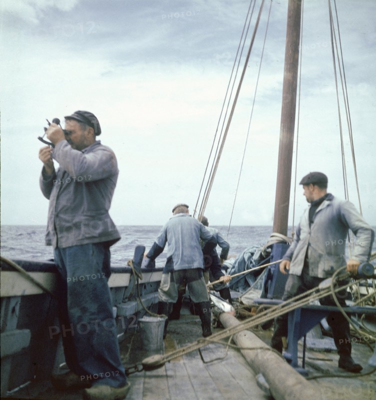 En 1955, en pleine mer, COLS, le patron du dernier thonier à voile de Concarneau prend une "hauteur" : à l'aide d'un sextant, il mesure la position du bâteau. A droite, FANCHE est à la barre.
