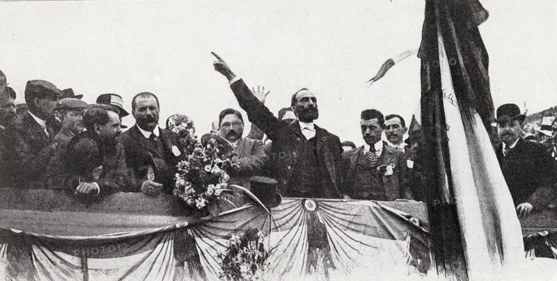 Meeting de Carcassonne, le dimanche 26 mai 1907. Harangue de l'organisateur Marcelin Albert devant près de 250 000 vignerons.   "On acclama frénétiquement Marcelin Albert, le promoteur, le Pierre l'Ermite de la croisade viticole, qui, modeste petit vigneron de la commune d'Argeliers, dans l'Aude, a réussi, par sa foi communicative et sa volonté opiniâtre, à mobiliser une armée de protestataires."  Photographie et extrait d'article parus dans L'Illustration du 1er juin 1907.  Devant l'impuissance des pouvoirs publics à juguler la grave crise qu'ils  traversent (surproduction et effondrement du prix du vin depuis 1904), les viticulteurs du Midi, menés par Marcelin Albert, organisent des meetings dans les principales villes de la région pour crier leur misère et réclamer des mesures contre les fraudes de toutes sortes commises sur les vins.