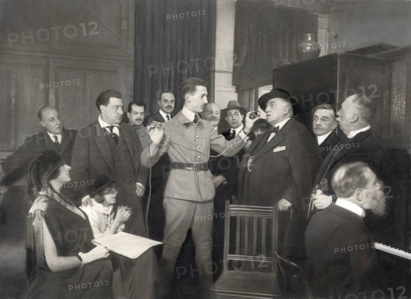 La T.S.F, un concert par téléphone sans fil le 26 novembre 1921. Dans le bureau du commandant Julien, chef du poste de radiotélégraphie de la Tour Eiffel : M Guitry Lucien dit des vers devant un combiné de téléphone pour deux mille auditeurs qui l'écoutent dans la salle du théâtre Municipal de Lille, en présence de Mlle Hatto, Madame Yvonne Printemps, M Sacha Guitry, le capitaine Bergeron, M Dutreux, M Lucien Guitry, M Georges Peutat, M Fernand Rivière au piano et M Alfred Brun, debout.