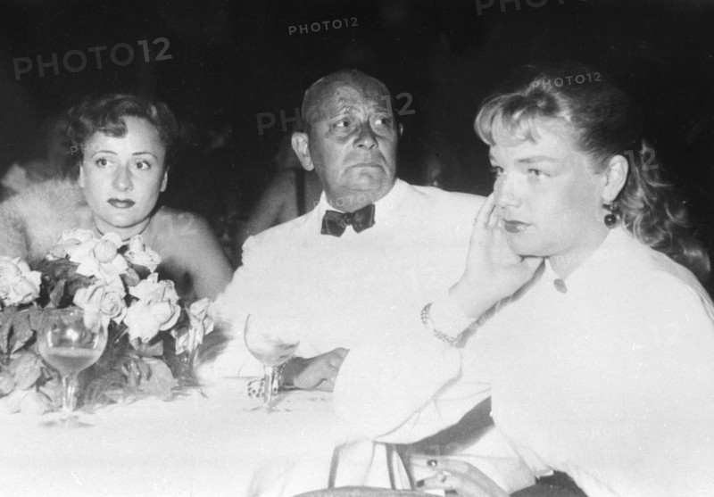 Soirées du Festival de Cannes de 1949.  L'acteur et réalisateur américain Eric von Stroheim entouré de son épouse Denise Vernac (à gauche) et de l'actrice française Simone Signoret. Photographie parue dans France-Illustration du 24 septembre 1949.