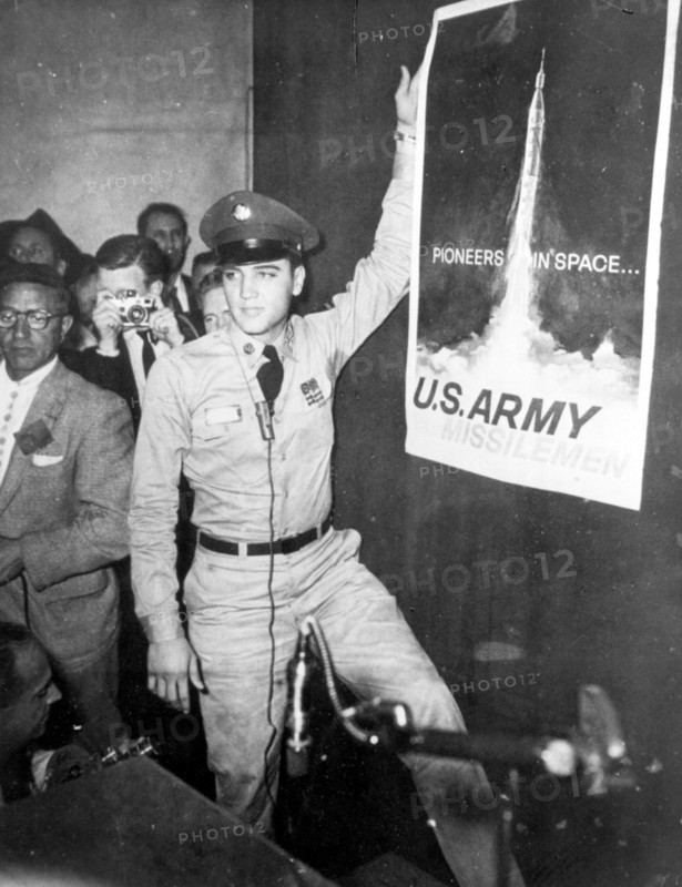 Elvis PRESLEY as a soldier next to the poster 'Pioneers in Space' 1958