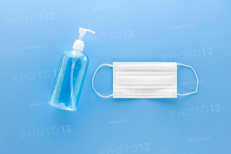 White medical mask and alcohol hand gel sanitizer to protect from virus and grem top view on blue background