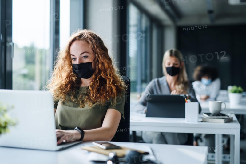 Young people with face masks back at work or school in office after lockdown.