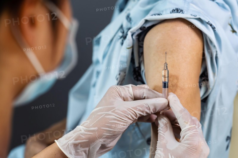 close up doctor in gloves holding syringe and making injection to patient in medical mask. Covid-19 or coronavirus vaccine