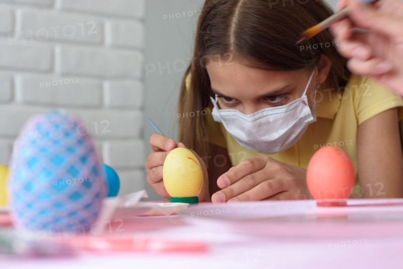 Close-up of a girl in a medical mask who paints Easter eggs