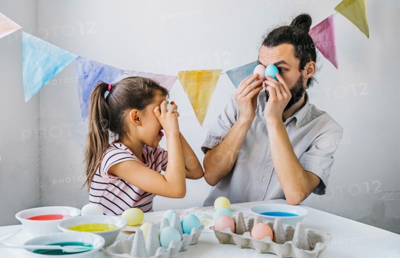 Happy family preparing to Easter celebrate at home. Adorable little girl and her having fun while while dyed easter eggs.