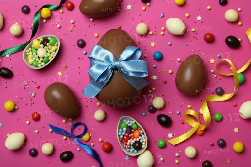 Easter chocolate eggs, candies and sprinkles on pink background