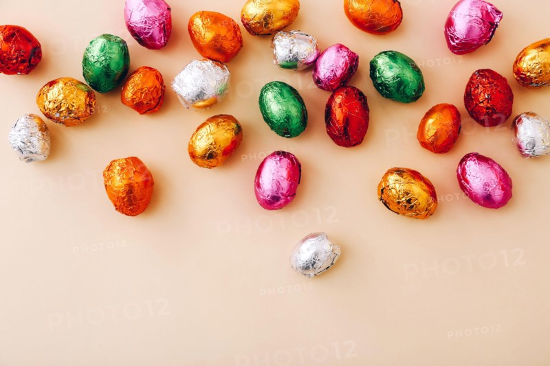 Easter chocolate mini eggs wrapped in a colorful foil, scattered on a beige background, top view, copy space.