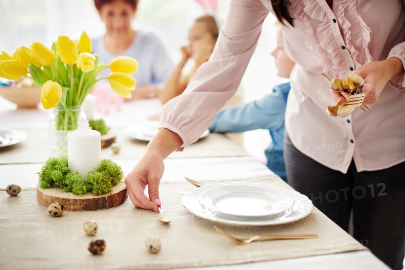 Woman and family preparing place settings at easter dining table