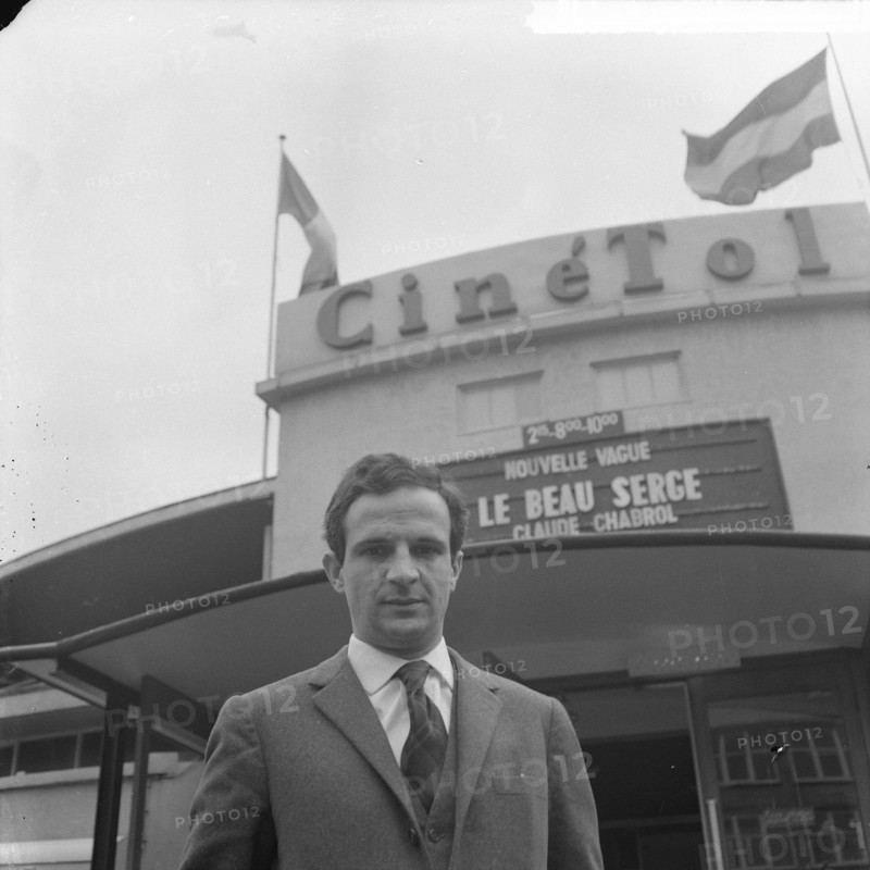 French director Francois Truffaut for cinema Cinétol, where his film plays [Le Peau Douce?] during Nouvelle Vague festival [on billboard film by Claude Chabrol Le Beau Serge] Date: 15 March 1965 Location: Amsterdam, Noord-Holland Keywords: cinemas, films, portraits, directors Personal name: Cinetol, Truffaut, François