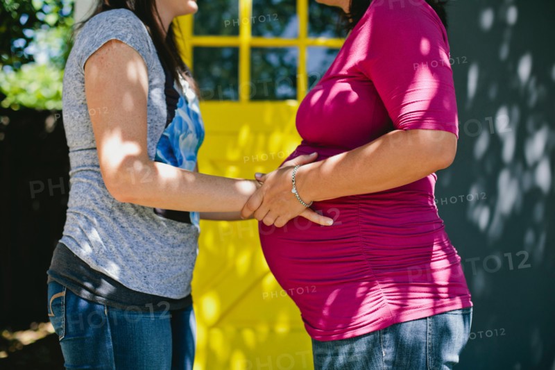 Woman touching pregnant girlfriend's belly while standing in backyard