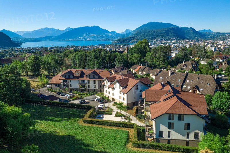 Complex of houses with mountains and large lake in distance. Aerial view of residential real estate in Annecy, France