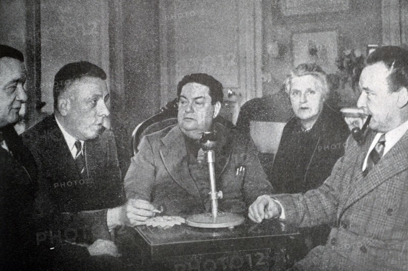 Black and white photograph of Darius Milhaud (1892-1974), French composer, at an evening party with French pianist and teacher Marguerite Long (1874-1966), French composer and pianist Francis Poulenc (1899-1963), French composer Georges Auric (1899-1983), and Swiss composer Arthur Honegger (1892-1955).