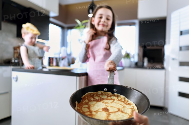 Cheerful siblings making crepes in the rustic home kitchen