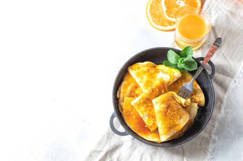 Crepes with Orange Sauce in a cast iron pan. Traditional French crepe Suzette with orange sauce.
