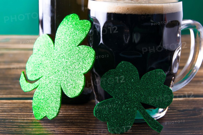 Close-up of two shiny clover leaves on a mug of stout. St. Patrick and stout concept