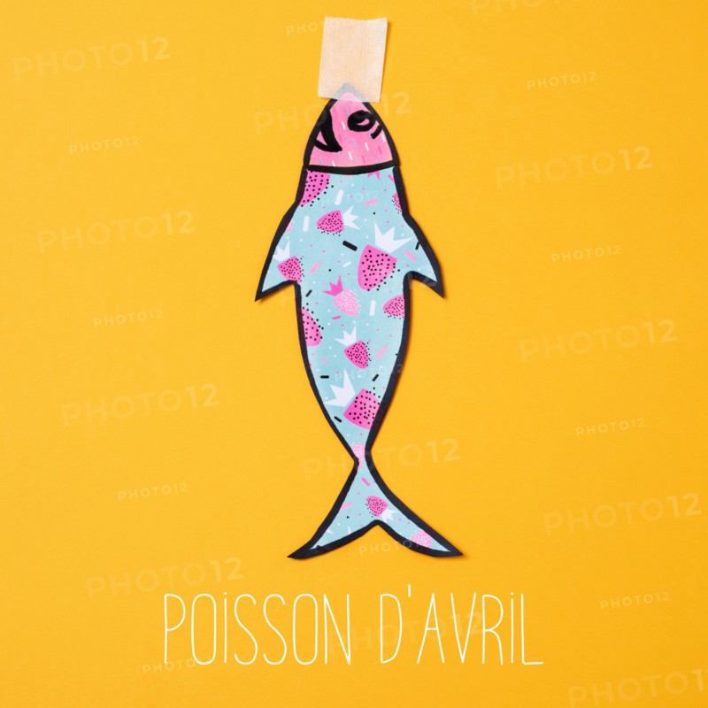 a homemade paper fish, made by myself, attached with adhesive tape to an orange background and the text poisson d avril, april fools day in french