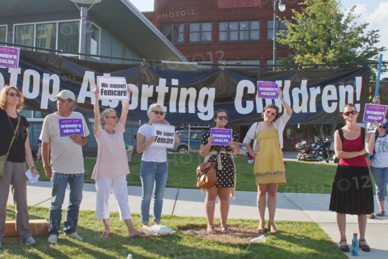 People hold pro women's health care and abortion signs in front of a large anti-abortion banner at a Moral Monday rally