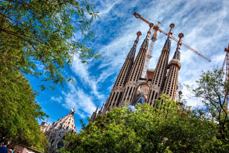 BARCELONA, SPAIN - MAY 13, 2017: The Sagrada Familia surrounded by trees and a beautiful blue sky, viewed from the Gaudi Square.