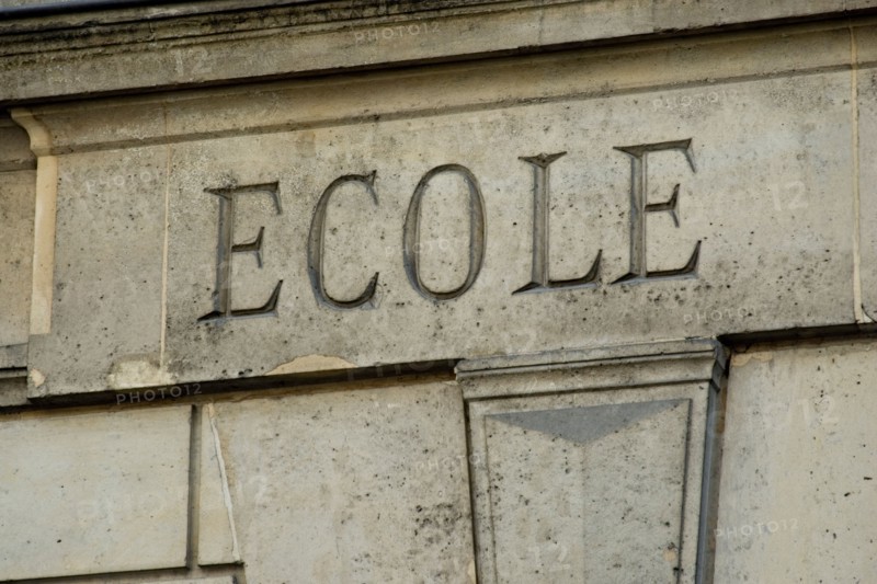 The word ECOLE engraved in stone on the facade of an old building in France