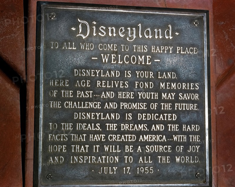 A dedication plaque commemorates the grand opening of the world’s most famous theme park, Disneyland, on July 17, 1955, in Anaheim, California, USA.  The metal tablet features a welcome “to this happy place” by Disneyland’s namesake creator, Walt Disney, who read the inscription to thousands of first-day guests and a nationwide audience during a ceremony on live television.  Today’s park visitors will find the plaque at the base of the pole flying the American flag at the south end of Main Street, U.S.A.