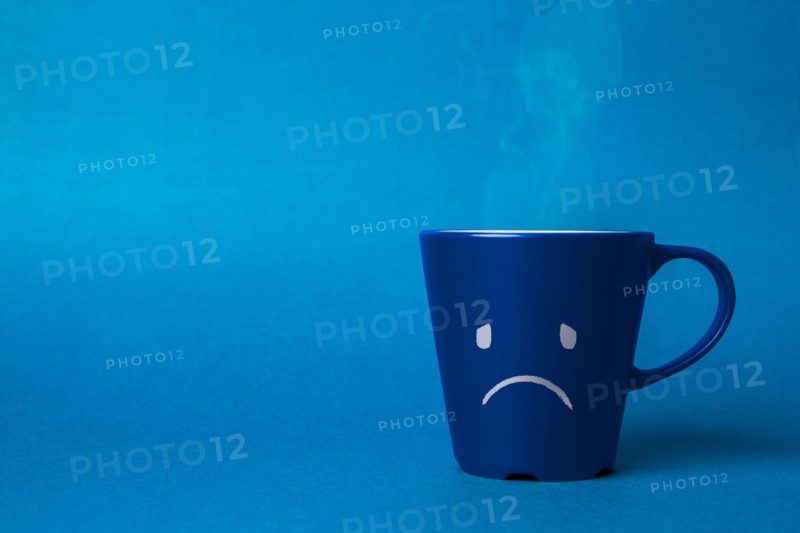 Stock photo of a blue cup on a blue background with a sad face drawn. Blue monday concept