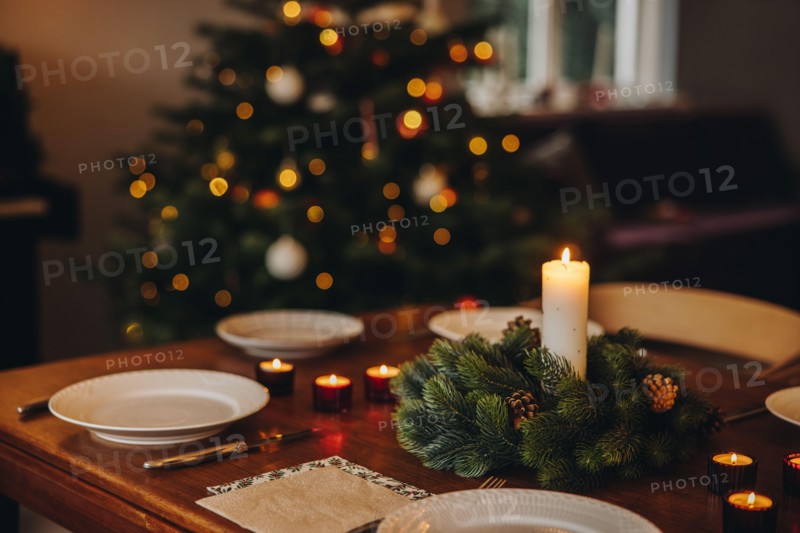 Christmas candles in advent wreath with plates on dinner table. Scandinavian home decorated for Christmas dinner.