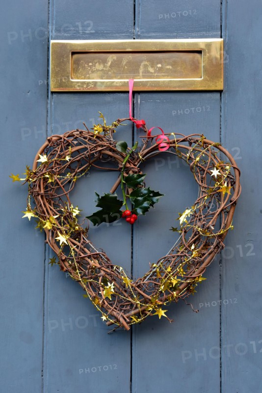 Christmas heart-shaped decoration hangs from festive red ribbon on a wooden door in the picturesque town of Ludlow, Shropshire, England, UK.