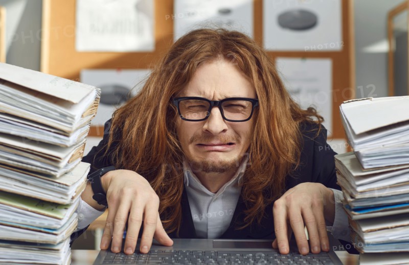 Funny unhappy office worker sitting at desk and crying stressed by huge workload