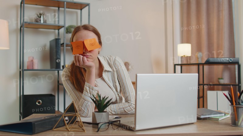 Tired woman teacher using laptop computer with funny stickers on eyes sleeps at workplace, napping