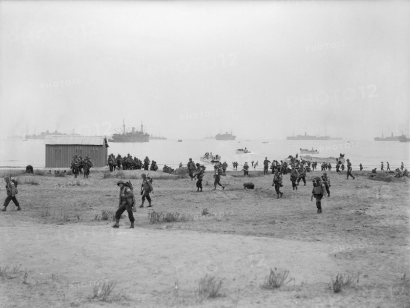 The Royal Navy during the Second World War- Operation Torch, North Africa, November 1942 American troops making their way inland after landing at Arzeu. Several small landing craft can be seen in the foreground whilst in the distance can be seen some of the troopships that helped transport the men.