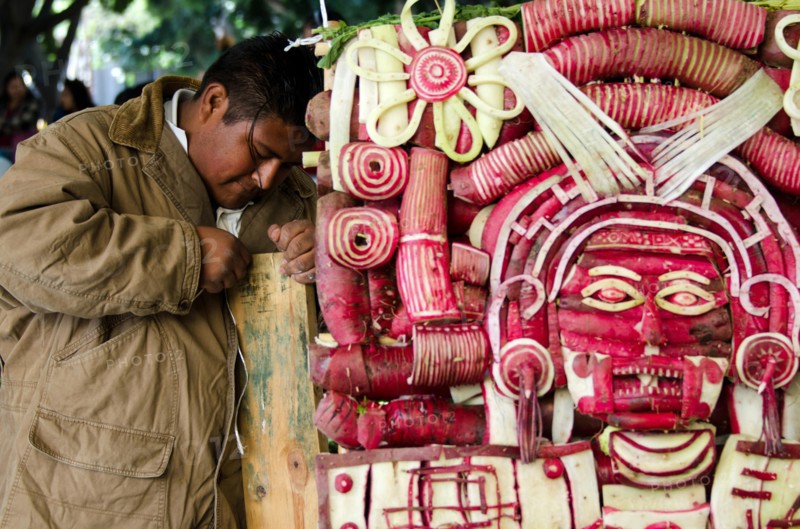 Young man carving Mixtec God of Death mask sculpture at Noche de Rabanos / Night of the Radishes festival, Oaxaca, Mexico.