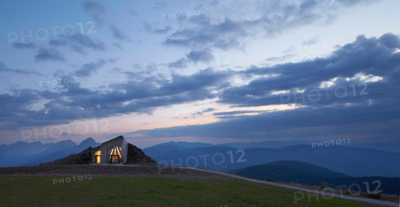 Distant view towards illuminated entrance at dusk. Messner Mountain Museum Corones, Mount Kronplatz, Italy. Architect: Zaha Hadi