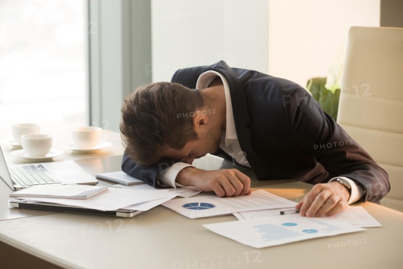 Tired young businessman sleeping on desk in office