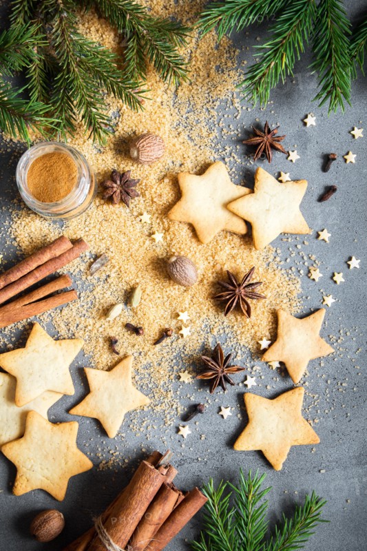 Christmas spices, gingerbread cookies and baking ingredients on grey concrete background. Cinnamon, anise stars, nutmeg, cardamon, cloves, brown sugar