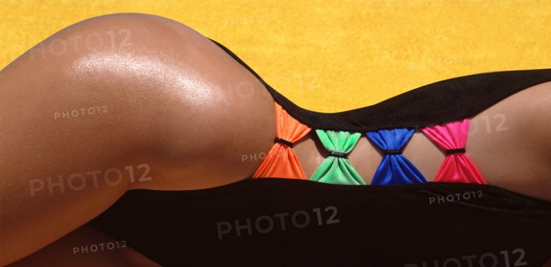 Historical 1988 archival model released abstract view of female  body curve shape created from a 1980s high cut on the thigh for woman fashion swimwear garment purchased in UK featuring close up detail of coloured bows connecting each black side of swimsuit against background of yellow towelling 80s archive outdoor image of how we were when photographed in Spanish holiday sunshine