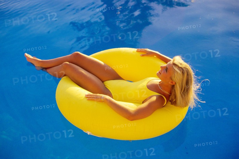 1980s BLOND WOMAN IN YELLOW BATHING SUIT ON YELLOW FLOAT IN SWIMMING POOL