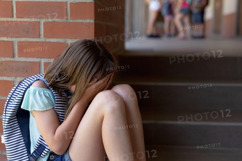 schoolgirl sitting and crying on the ground alone in the schoolyard at elementary school