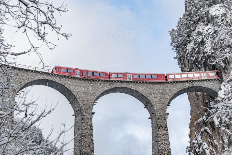 The Landwasser Viaduct with famous train of red color at winter time, landmark of Switzerland, snowing, Glacier express