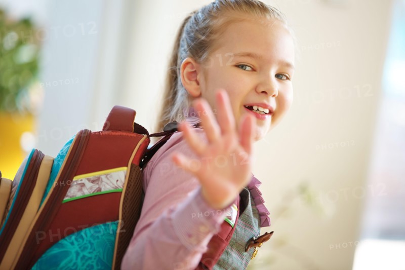 Smiling child with satchel goes to school and waves goodbye