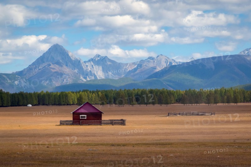House in the countryside with the mountains in the background. Farm cabin in the rural country surrounded by forest and hills with the snowy tops.