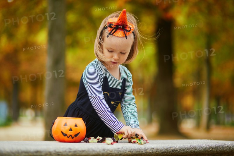 Adorable toddler girl in black cat dress with tutu skirt trick-or-treating with orange pumpkin bucket. Happy kid celebrating Halloween in Paris, Franc