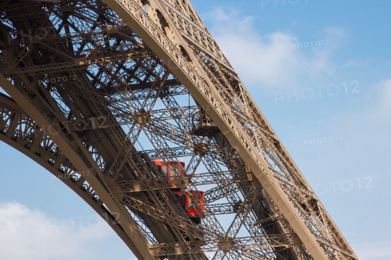 Two bright red elevators climbing up one of Eiffel Tower iron girders bringing tourists to the first floor