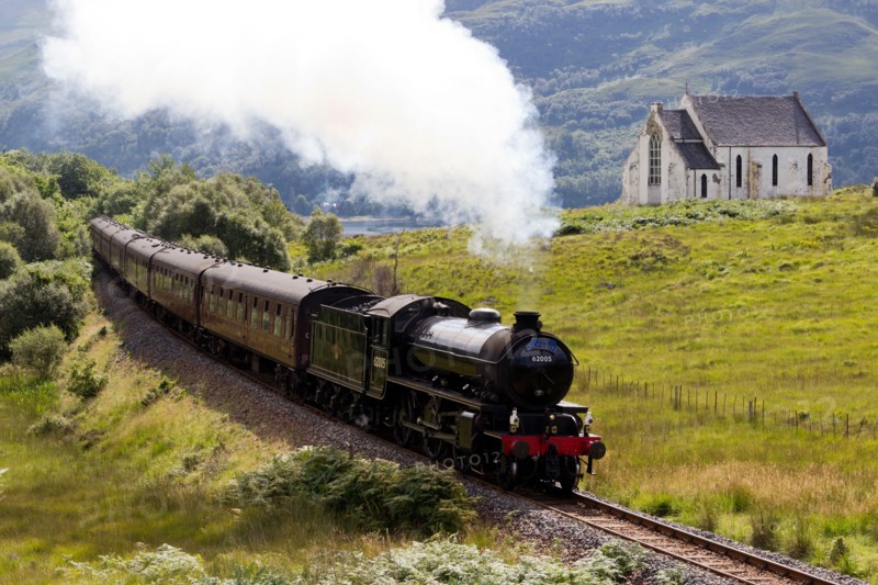 Jacobite Steam Train passing Our Lady of the Braes Church at  Polnish Highlands Scotland UK