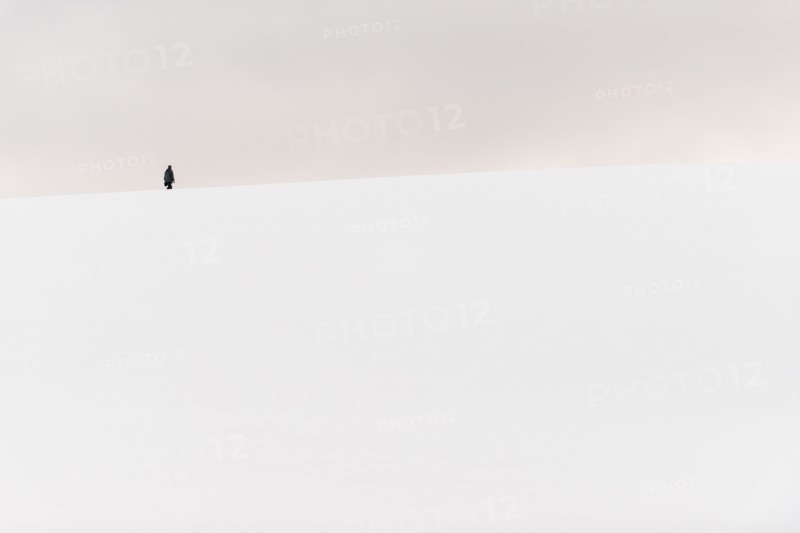 ANTARCTICA - A person hikes to the top of a small snow-covered hill in Hughes Bay on the western coast of the Antarctic Peninsula.